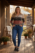 Plus size curvy woman wearing color block long sleeve pullover in taupe, black, and rust in a cozy autumn cabin setting