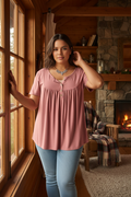 Plus size model wearing a button-up loose fit tee, standing by a rustic cabin window with warm natural light and cozy cabin decor in the background