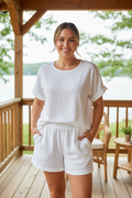 Plus size woman wearing white cotton linen t-shirt and shorts set with hands in pockets on a sunny cabin porch